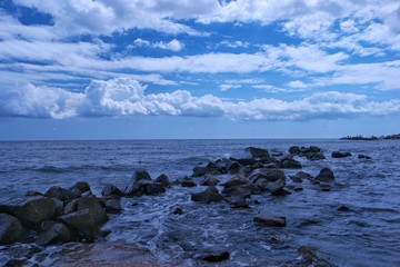 A view of an expanse of sea, the rocks and the waves against cloudy sky