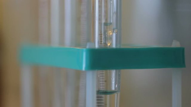 Laboratory experiment of ecology researches: close up shot of falling drops from pipette into glass vial. The vial has special marks in russian