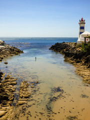 Fototapeta na wymiar Beautiful small beach of Santa Marta in Cascais - transparent water and lighthouse in the background