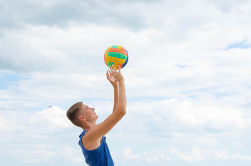 Portrait of a smiling volleyball player with colorfull ball at the cloudy sky background.