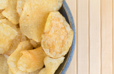 Top close view of a bowl of salt and vinegar flavored potato chips on a wood place mat.