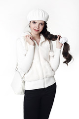 Fashion teen white style look. Fashionable young girl wears fur jacket and beret, holding handbag, posing isolated on studio background.