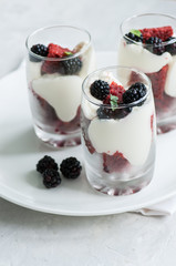 Red velvet sponge cake with cream cheese decorated with fresh blackberries - dessert in a glass on a white stone background.