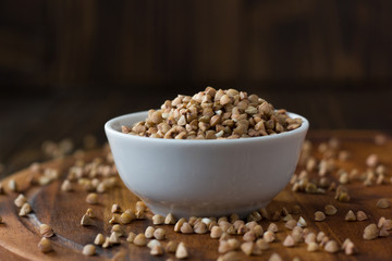 Buckwheat grain on ceramic bowl over wooden table.