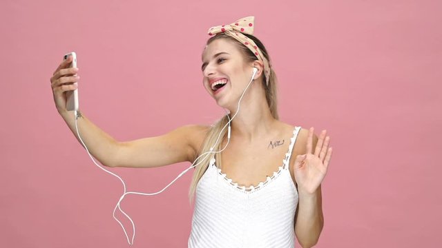 Young happy caucasian lady talking with friends by phone over pink background