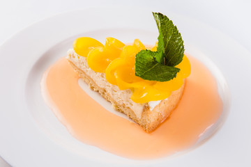 Peach cheesecake on a white plate on a light background (close)