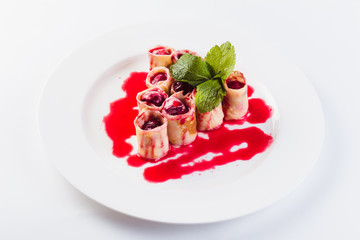 rolled pancakes stuffed with berries called white plate on a light background (close)