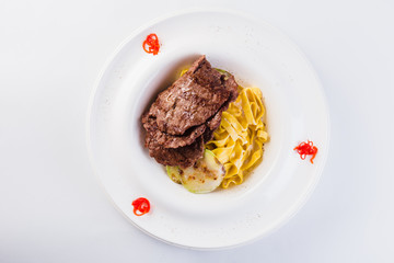 Tagliatelle with beef on a white round plate on a light background