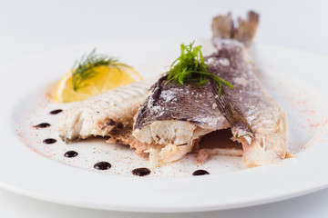grilled dorada in salt with lemon slice on a white plate on a light background (close)