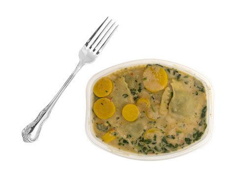 Top view of a ravioli with spinach TV dinner with a fork to the side isolated on a white background.