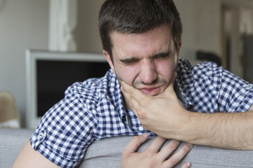 Toothache. Frustrated young man touching his cheek and keeping eyes closed