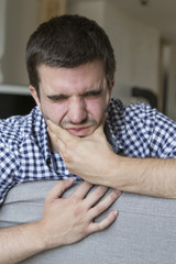 Toothache. Frustrated young man touching his cheek and keeping eyes closed