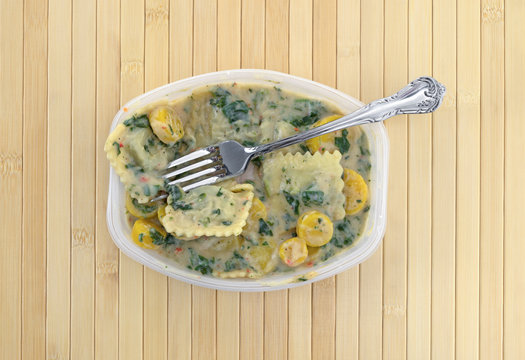 Top view of a ravioli with spinach TV dinner with a fork on the food atop a wood place mat.