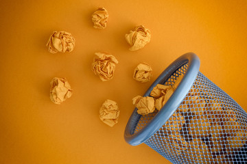 Yellow crumpled paper balls rolling out of a trash can