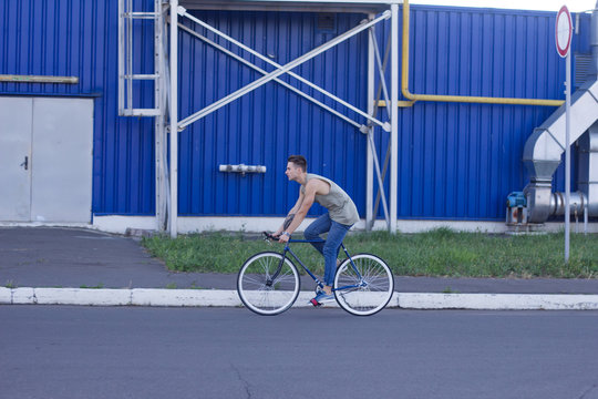 Young ,man ride on fixie bike, urban background, picture of hipster with bicycle in blue colors 