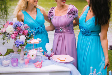 Bridesmaids are hugging and laughing near the festive table at the ceremony. Wedding decoration in the style of boho, floral arrangement in the garden.