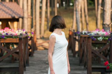 Beautiful happy young woman in white dress dancing on wooden platform near forest outdoors. Beautiful warm summer day