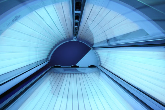Solarium empty tanning bed in modern beauty salon, view from inside with closed lid and all light bulbs glowing on. Concept of sunbath, beauty lifestyle and healthcare