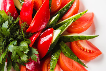 Vegetable salad - tomato, pepper, cucumber  and greens on a white plate on a light background (top view  close)