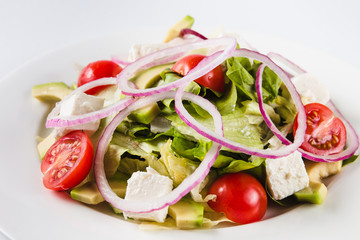 Salad with arugula and tomatoes on a round white plate on a light background (close)