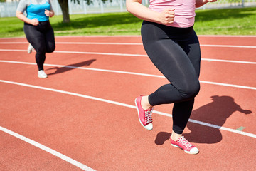 Low section of chubby female in activewear running on racetrack of stadium