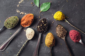 Obraz na płótnie Canvas Beautiful colored spices in a silver spoon on a dark background. The concept of cooking, healthy food