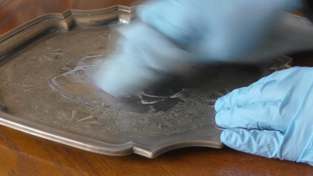Man with gloves polishing an antique silver tray
