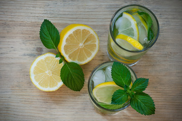 Refreshing drink with water, lemon, mint, ice in glasses on a wooden background. Homemade detox water