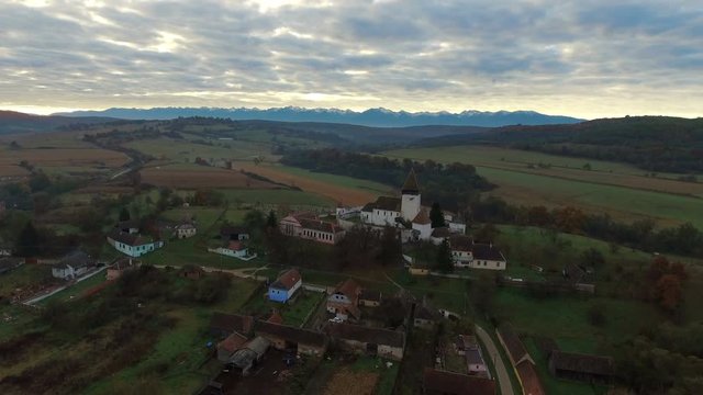 Aerial drone slow shot over transylvanian village with saxon houses and green valleys.	Autumn countryside view in foreground and Fagaras Mountains in background. Transylvania, Romania. 4k footage. 