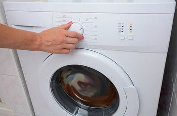View on how a woman is turning on of the washing machine. A woman is choosing a washing mode on the washing machine.