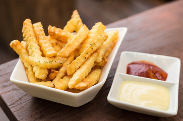 French fried in white bowl with tomato sauce and mayonnaise on wooden table