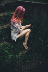 The beautiful girl with pink hair sits on the thrown ladder in an environment of a green grass