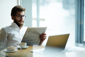 Seerious man reading vacancy adverts in newspaper