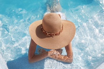 Woman in beach hat enjoying in swimming pool on luxury tropical resort. Exotic Paradise. Travel, Tourism and Vacations Concept.