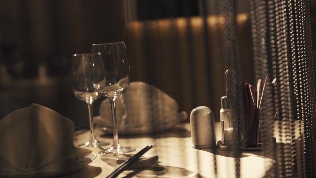 Plates with tissues, wine glasses and chopsticks served on dining table behind curtain in chinese restaurant