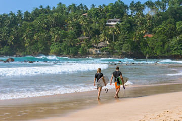 The beach and bay of Mirissa. Surfers with their boards on their way to the waves. The beach on the south coast is very popular with surfers. It is a top spot for water sports.