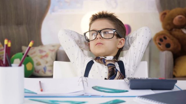 Small child boy in white shirt and tie images he is smart businessman working with papers and calculator, making notes, like adult professional, dreaming to be as his father, sitting at the table