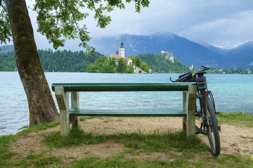 Bicycle leaning on the bench on the bank of Bled lake on a summer day.