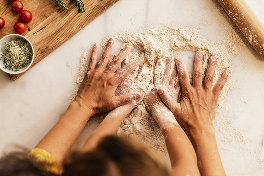 Little girl kneading flour with her mother.