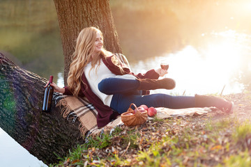 Beautiful woman drinking wine outdoors having picnic in the park. Portrait of young blonde beauty...
