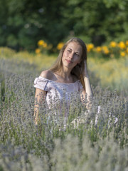 Beautiful woman in sunny day wearing pink dress and sitting in fresh lavander field, enjoying beauty of nature