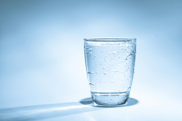 Glass with water and water drops on a blue background