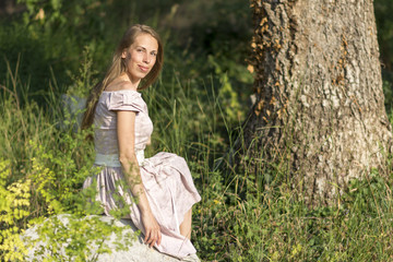 Naklejka na ściany i meble Beautiful girl in the field. Women sits on a rock, enjoying the outdoors and the sun.