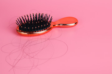 Hairbrush or Comb with some hair on its showing the hair fall problem on pink background. 