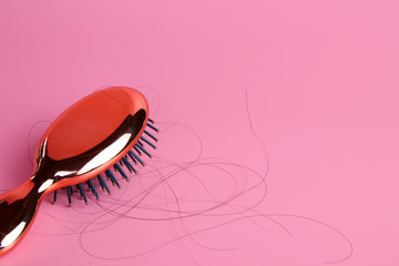 Hairbrush or Comb with some hair on its showing the hair fall problem on pink background. 