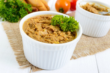 Delicate pate from chicken liver in ceramic bowls on a white wooden background.