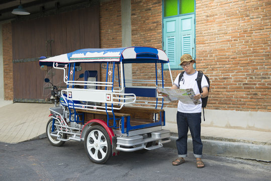 Asian man traveler is using local map while traveling in South East Asia with vintage taxi bike style.