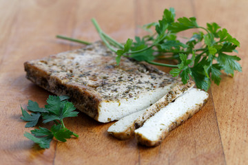 Block of marinated tofu with herbs, two tofu slices and fresh parsley  on wooden chopping board.