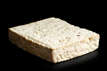 Single block of lightly smoked tofu isolated on black.