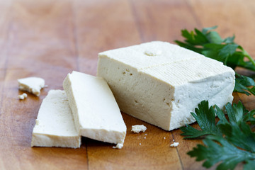 Single block of white tofu with two tofu slices, crumbs and fresh parsley  on wooden chopping board.